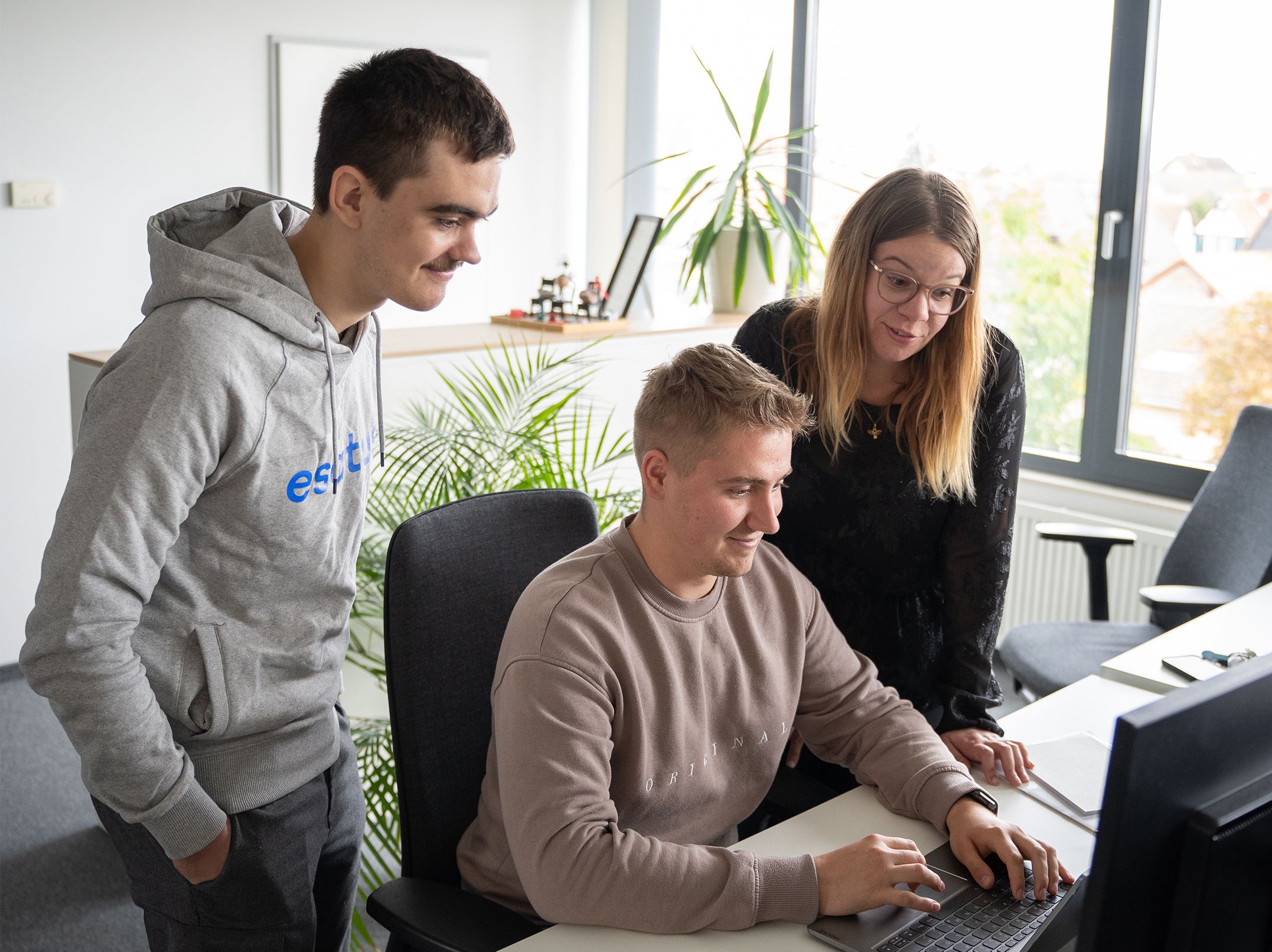 Three esatus team members discussing AI-assisted software development at a laptop